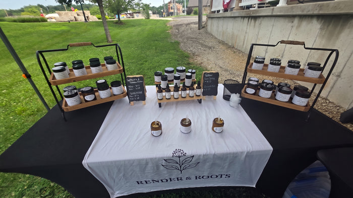Render & Roots booth at a local farmers market with tallow balms, whipped butters, and beard oils on tiered wood displays